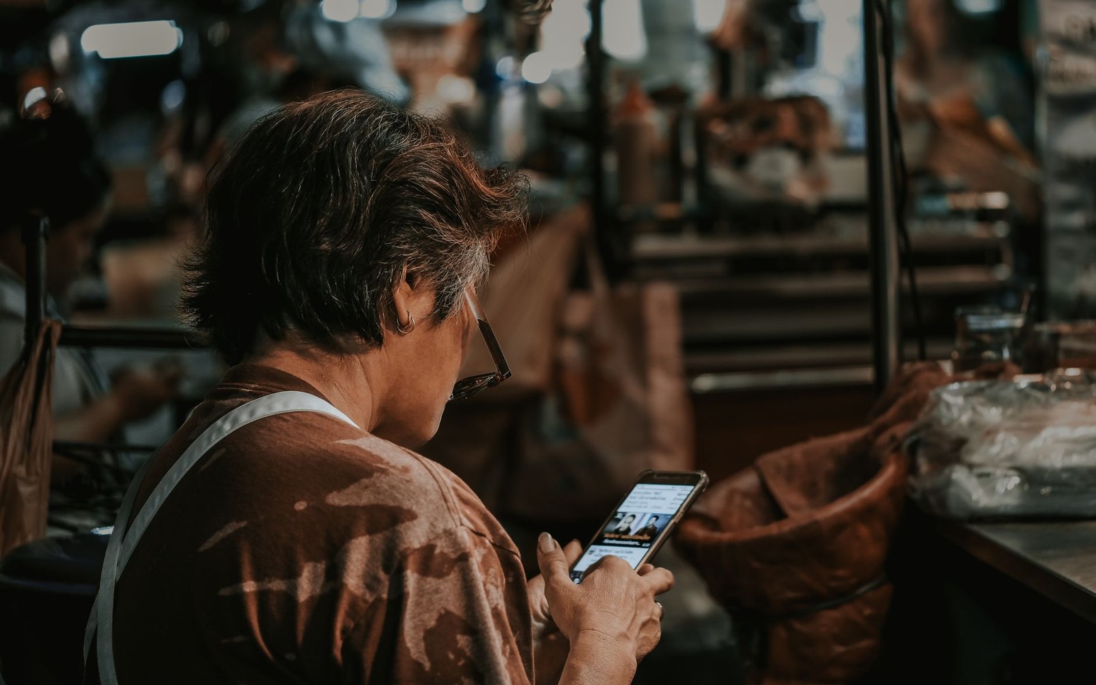 An adult looking at a smartphone screen in an indoor public space, the phone screen bright against the ambient light, face visible and in focus