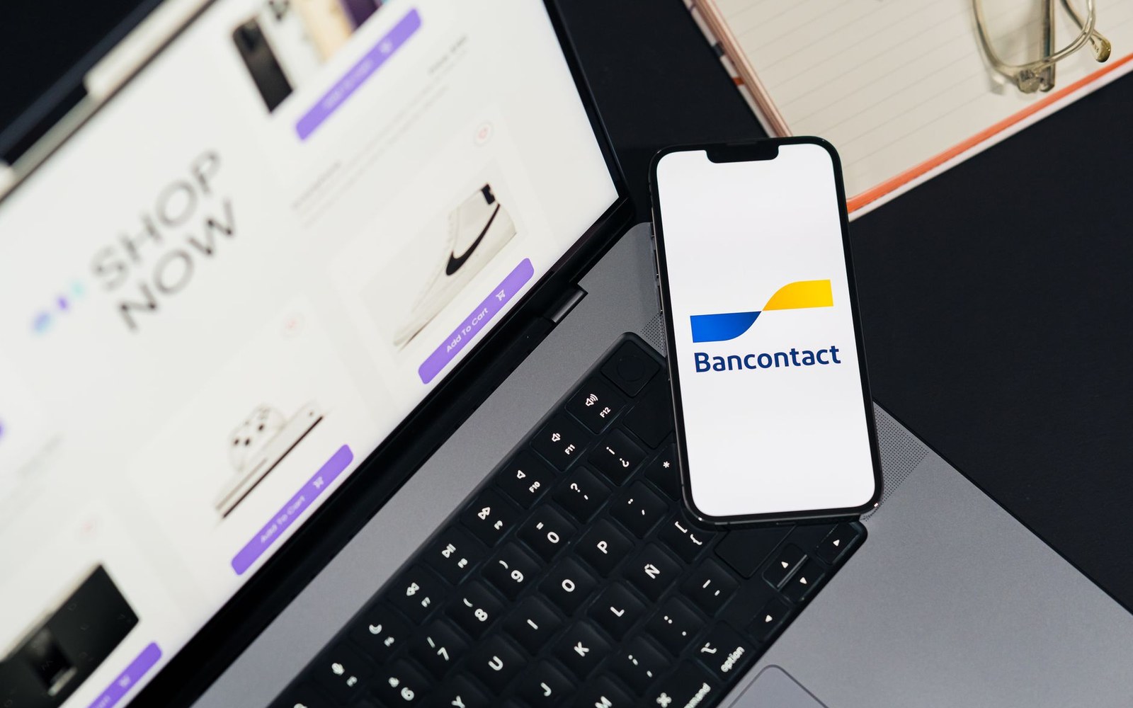 Phone showing the Bancontact logo resting on a laptop keyboard next to a shopping website