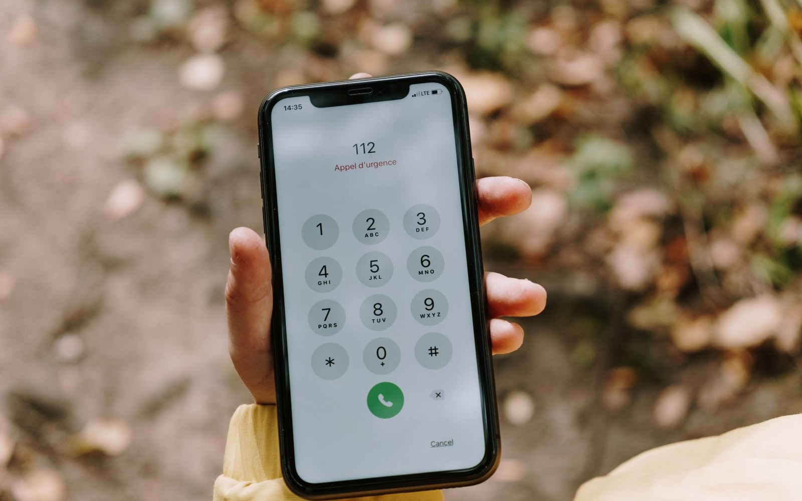 A hand holds a smartphone outdoors showing the emergency dialer with 112 entered