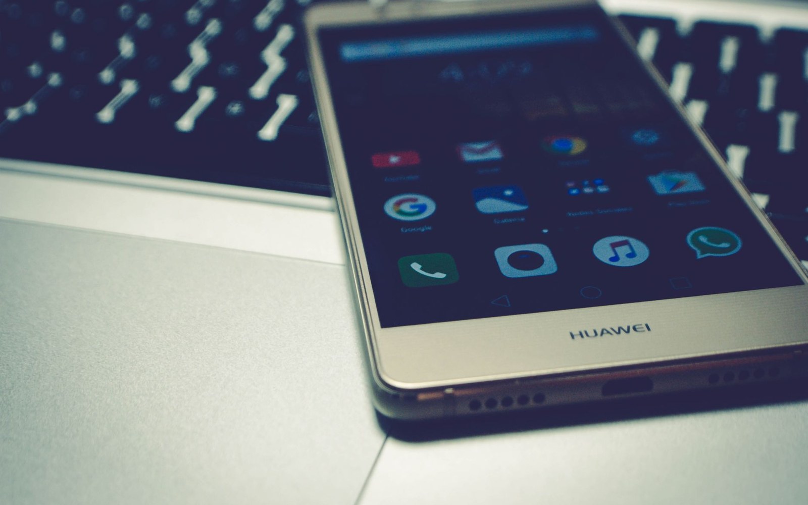 Huawei smartphone displaying app icons on its home screen, resting on a laptop keyboard