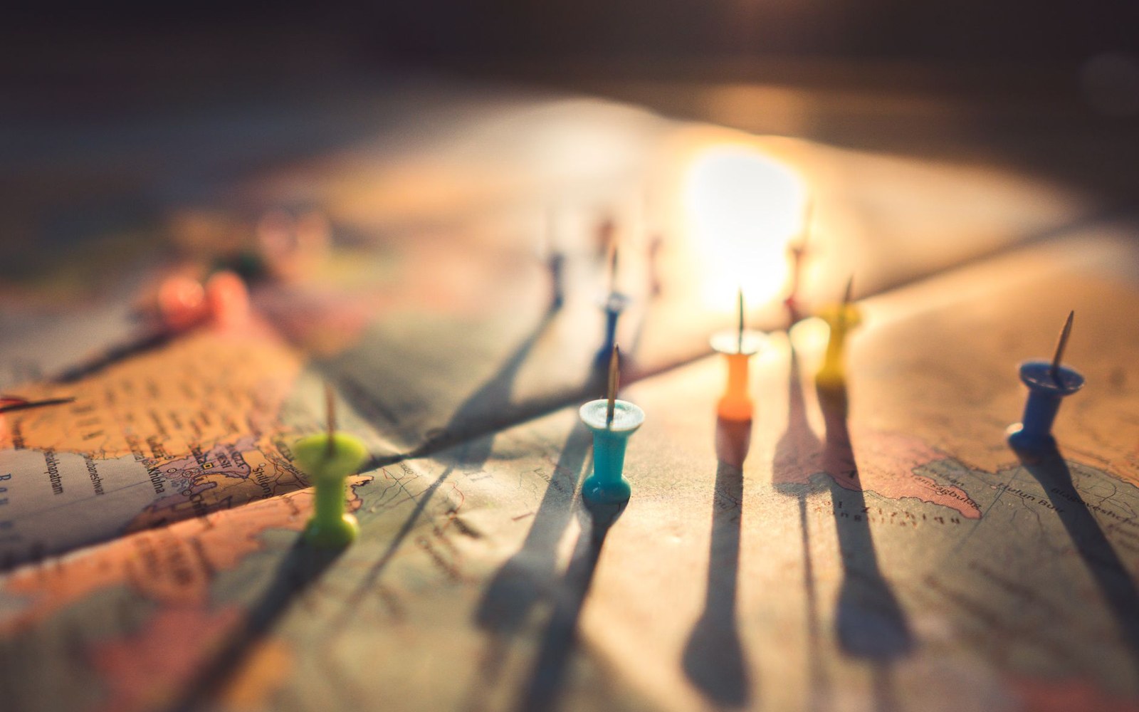 Colorful pushpins mark scattered locations across a paper map lit by warm backlight
