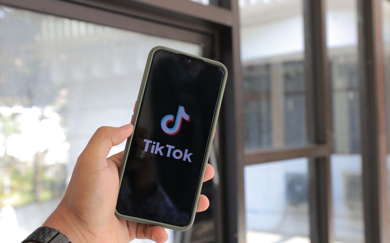 A hand holds a smartphone displaying the TikTok logo on its loading screen