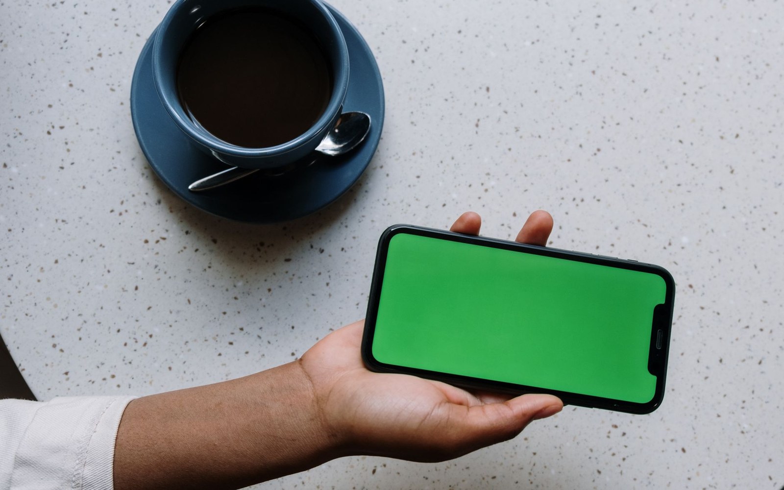 An adult hand holding an iPhone showing an app store listing, the phone photographed from directly above, placed across the vertical frontier line dividing the near-black outside field from the warm paper inside field
